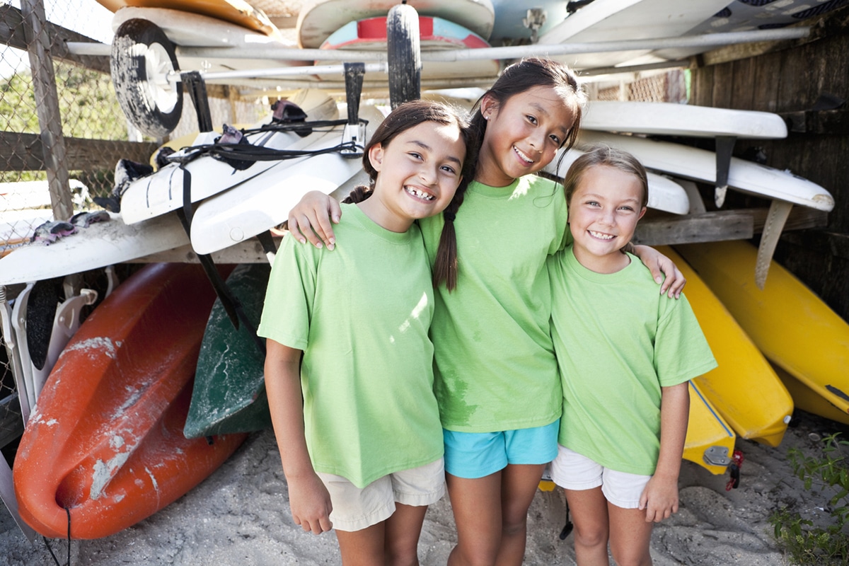 Three young campers posing in front of a kayak stand